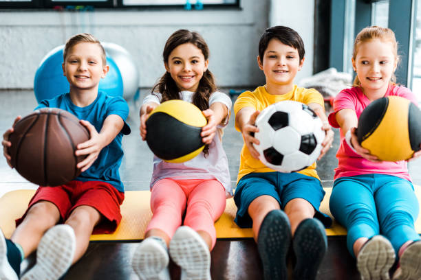 niños alegres sentados en un estera de fitness con pelotas - sports equipment fotos fotografías e imágenes de stock