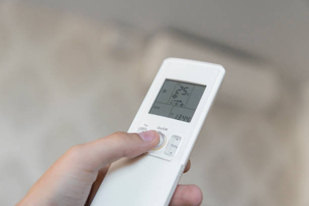 istock Hand with remote control directed on the conditioner on the wall. Man's hand using remote control open The air conditioner is cooled to 25 degrees Celsius in his bedroom. 1151210442