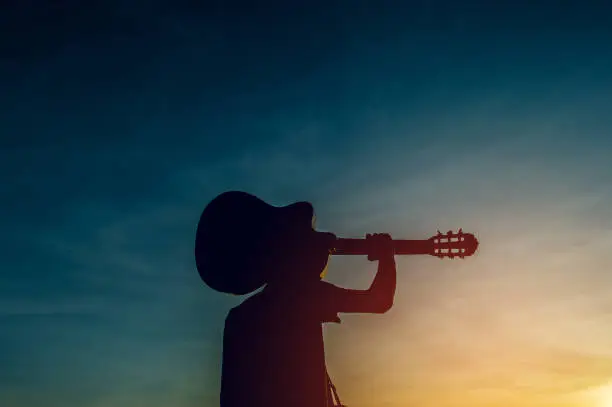 Photo of Silhouette of a guitarist in the shadows at sunset light, silhouette concept.