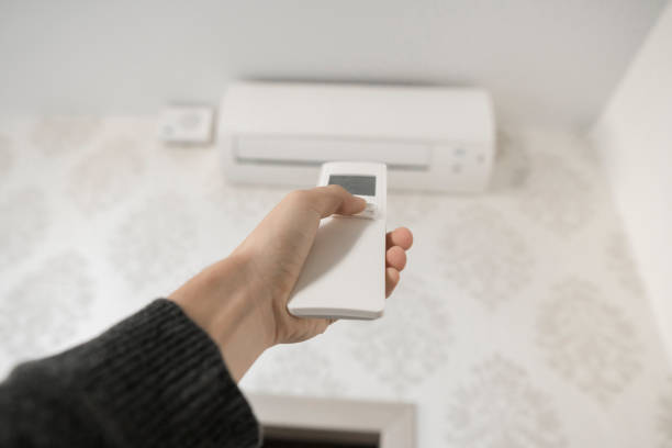 istock Hand with remote control directed on the conditioner on the wall. Man's hand using remote control open The air conditioner is cooled to 25 degrees Celsius in his bedroom. 1151210804