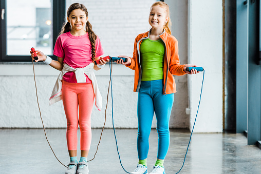 Adorable children training with skipping ropes in gym