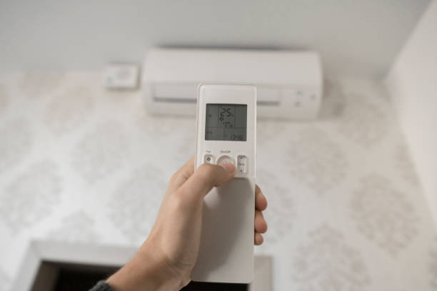 istock Hand with remote control directed on the conditioner on the wall. Man's hand using remote control open The air conditioner is cooled to 25 degrees Celsius in his bedroom. 1151214136