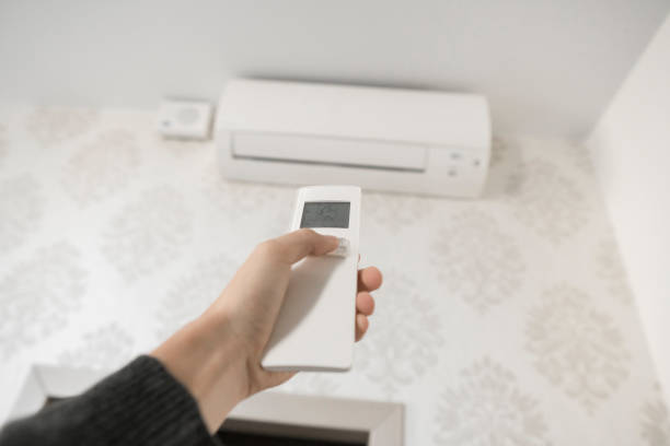 istock Hand with remote control directed on the conditioner on the wall. Man's hand using remote control open The air conditioner is cooled to 25 degrees Celsius in his bedroom. 1151215064
