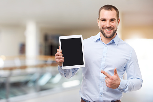 Happy businessman in blue shirt shows touch screen in a business center