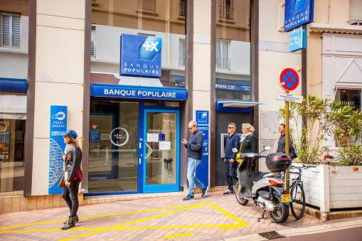 Biarritz, France - May 04, 2019: People sightseeing and shopping in Biarritz city center, France. Banque Populaire with ATM outside and motorcycle parked