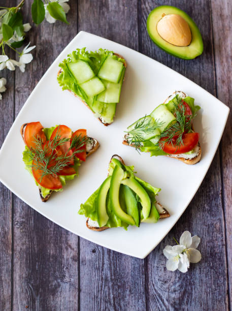 Vegetarian sandwiches with avocado, tomatoes and cucumbers on a wooden background