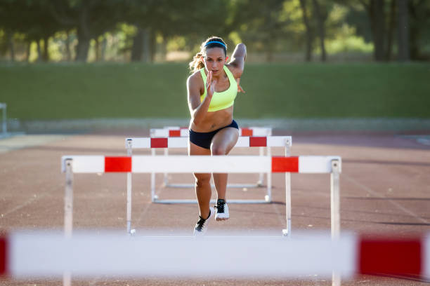 Young athlete jumping over a hurdle during training on race track. Portrait of young athlete jumping over a hurdle during training on race track. track and field stock pictures, royalty-free photos & images