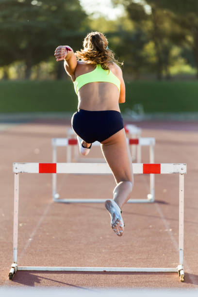 young athlete jumping over a hurdle during training on race track. - hurdling hurdle running track event imagens e fotografias de stock