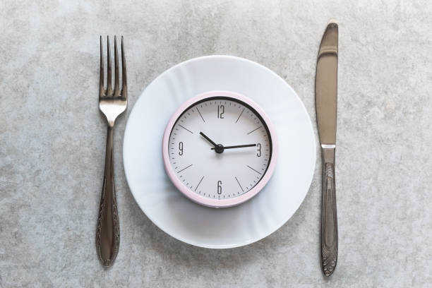 istock Pink alarm clock on a white plate with metal utensils. Dieting, eating concept. 1151237678
