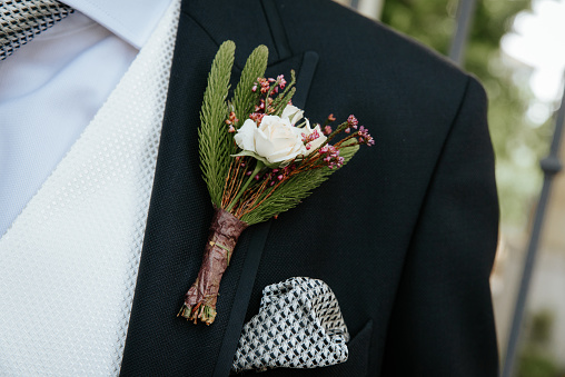 Boutonniere with a rose and sprig of fir on the background of the groom's jacket.
