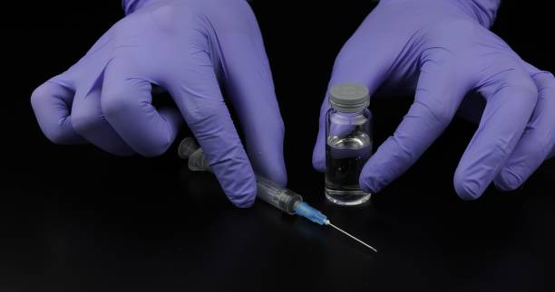 istock Doctor's hands with syringe, ampoule with vaccination on black background 1151264230
