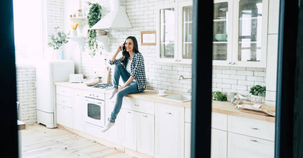 istock Beautiful cute smiling woman is using smart phone on the kitchen at home. 1151268530