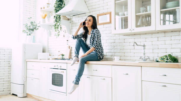 istock Beautiful cute smiling woman is using smart phone on the kitchen at home. 1151268540