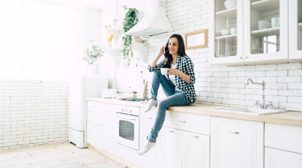 istock Beautiful cute smiling woman is using smart phone on the kitchen at home. 1151268543
