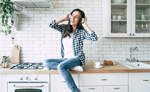 Relax at home. Beautiful happy young woman in headphones is listening music and have a fun on the kitchen.
