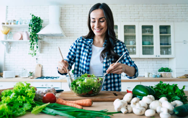 Beautiful cute young smiling woman on the kitchen is preparing a vegan salad in casual clothes. Beautiful cute young smiling woman on the kitchen is preparing a vegan salad in casual clothes. woman making healthy dinner stock pictures, royalty-free photos & images