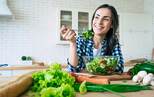 Un estilo de vida saludable. Buena vida. Comida orgánica. Verduras. Close up retrato de feliz linda joven hermosa mujer mientras intenta sabrosa ensalada vegana en la cocina en casa. photo