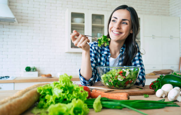 sain. bonne vie. des aliments biologiques. légumes. fermez le portrait de la belle jeune femme heureuse mignonne tandis qu’elle essaye la salade vegan savoureuse dans la cuisine à la maison. - healthy woman photos et images de collection