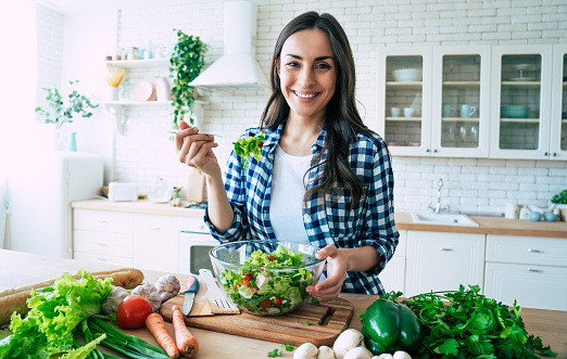 Healthy lifestyle. Good life. Organic food. Vegetables. Close up portrait of happy cute beautiful young woman while she try tasty vegan salad in the kitchen at home.