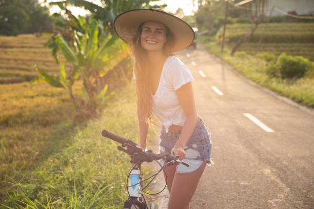 mulher com uma bicicleta na estrada secundária estreita - rice paddy rice food short grain rice - fotografias e filmes do acervo