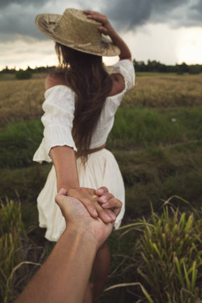 Man follows her woman. Couple holding hands in the rice field.