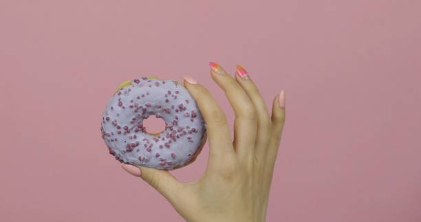 istock Womens hand holding blue, delicious, sprinkled donut on pink background. 1151276268