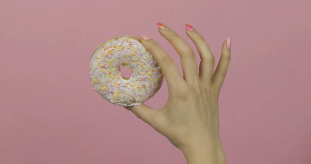 istock Womens hand holding white, delicious, sprinkled donut on pink background. 1151276301