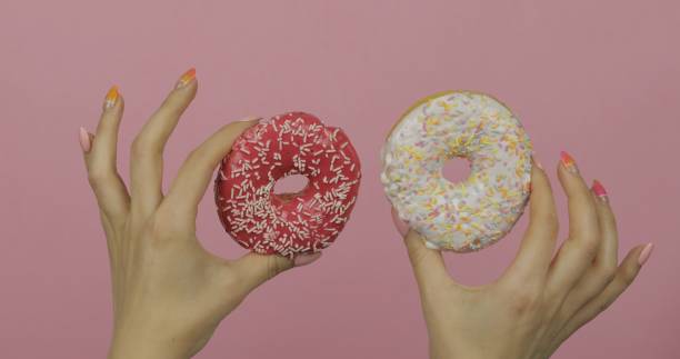 istock Womens hands holding two white and red, sprinkled donuts on pink background. 1151276321