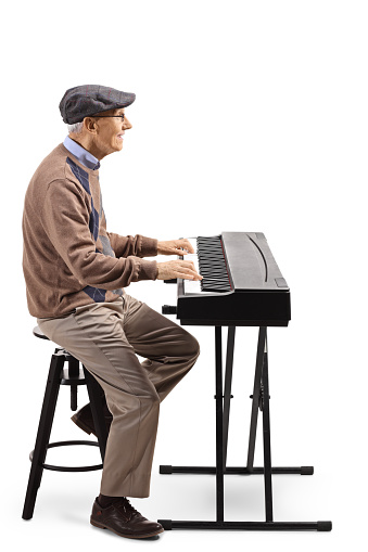 Full length profile shot of an elderly man playing a digital piano isolated on white background