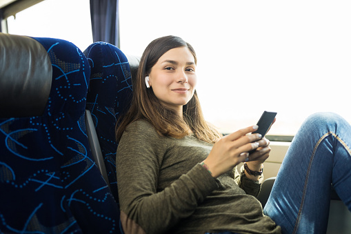 Smiling attractive woman listening music on smartphone while sitting in bus