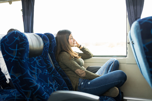 Thoughtful woman sitting comfortably on seat by window in bus