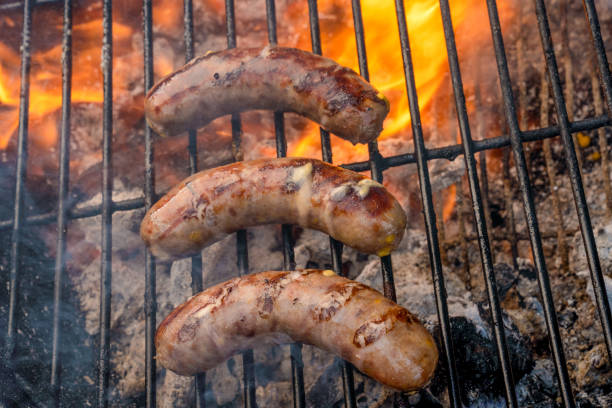 Four plump bratwurst cooking on an old fashioned charcoal grill