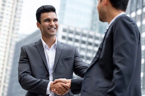 Young smiling Indian businessman making handshake with partner  in the city