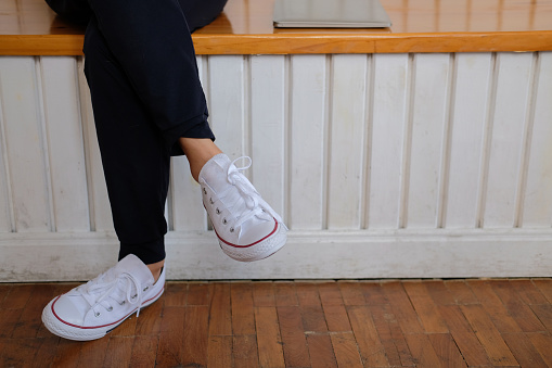woman feet wearing white sneakers sitting on wood bench