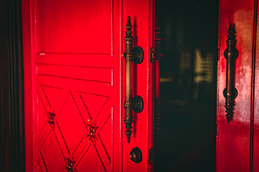 Old wood red double doors leading in to a dark hall.