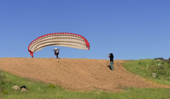 Female paraglider pilot taking off and woman filming with her mobile, with a blue sky in the background