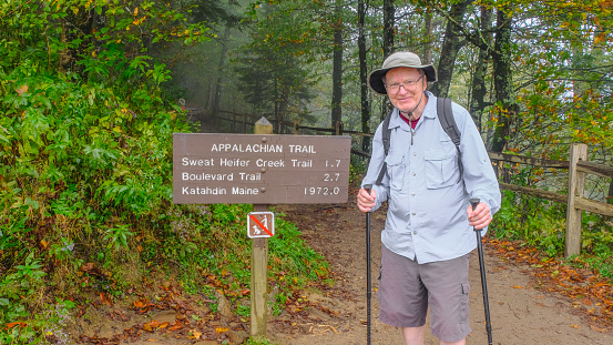 Smiling senior man standing next to Appalachian Trail sign; woods in background