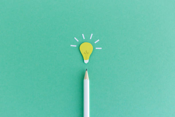 Pencil with light bulb above Creative composition of pencil with small paper light bulb glowing above on green background wisdom photos stock pictures, royalty-free photos & images