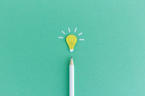 Pencil with light bulb above Creative composition of pencil with small paper light bulb glowing above on green background creative occupation stock pictures, royalty-free photos & images