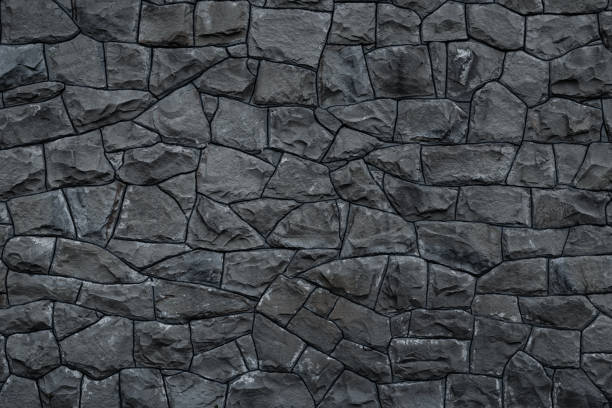 Gray dirty stone wall. Texture of grey granite. Dark rough rocks background. Weathered dark gray grunge building's facade. Stone surface. Mosaic pattern of grey stones on the cement wall. Old dirty wall rock texture. Grey backdrop of decorative tiles. stock photo
