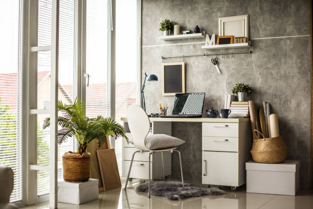 Interior of a modern office Interior of a modern home office next to a big window. Light wood desk with organized set up of books, office supplies and laptop with some room decor around it. good condition stock pictures, royalty-free photos & images