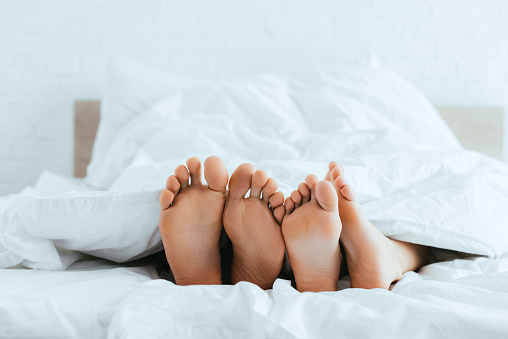 cropped view of boyfriend and girlfriend with barefoot lying in bed