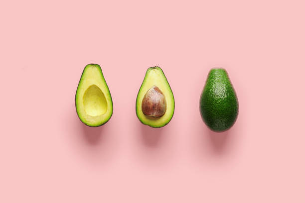 istock Whole avocado fruit and two halves in a row isolated on pink background 1151343076