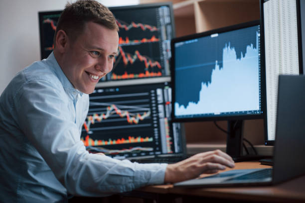 istock Smiling during the process. Man working online in the office with multiple computer screens in index charts 1151344241