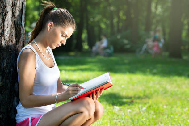 istock young brunette woman writing to notepad, leaning on a tree 1151347093