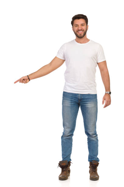 istock Young Man In Jeans And White T-shirt Is Standing, Smiling And Pointing. Front View 1151347298