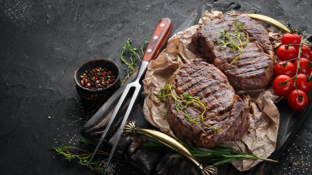 istock Grilled ribeye beef steak, herbs and spices on a dark table. Top view. Free space for your text. 1151348082
