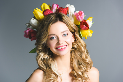 happy girl with wreath of flowers on hair isolated on grey