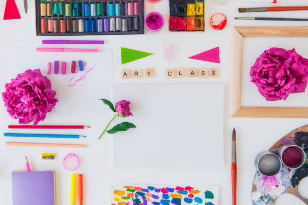 istock Top view creative artist workplace. Blank Canvas, Art class lettering on wooden blocks and various colorful painting materials and flowers on white background.Art therapy, Drawing lessons. Flat lay. 1151353348