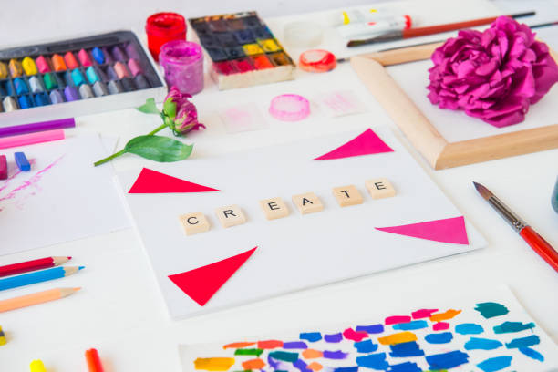Side view close up creative artist workplace. Blank canvas with Create word lettering, variety of painting supplies and peony flowers. Drawing, inspiration, craft, creativity concept. Art therapy.